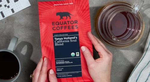 New red packaging of Equator Coffees on grey table next to cups of coffee