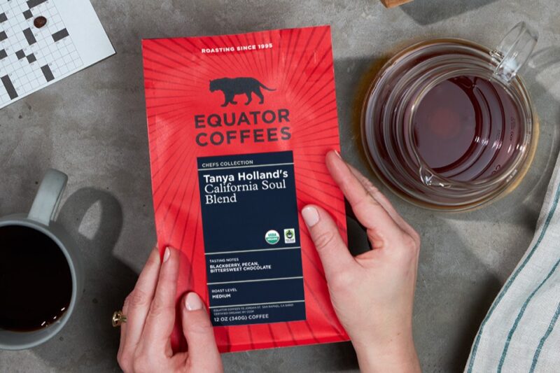 New red packaging of Equator Coffees on grey table next to cups of coffee