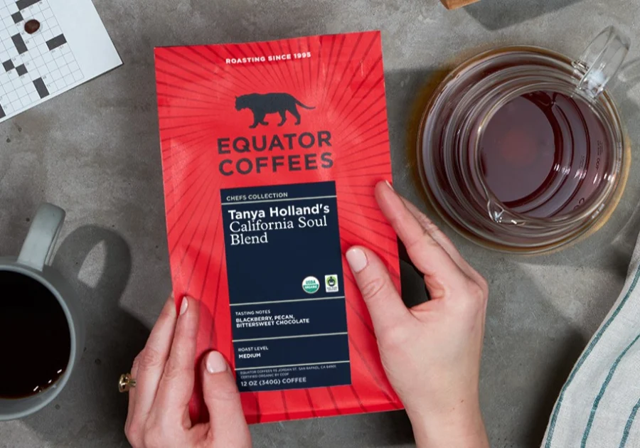 New red packaging of Equator Coffees on grey table next to cups of coffee