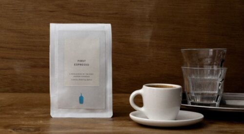 Bag of coffee, espresso cup and water glasses on a table.