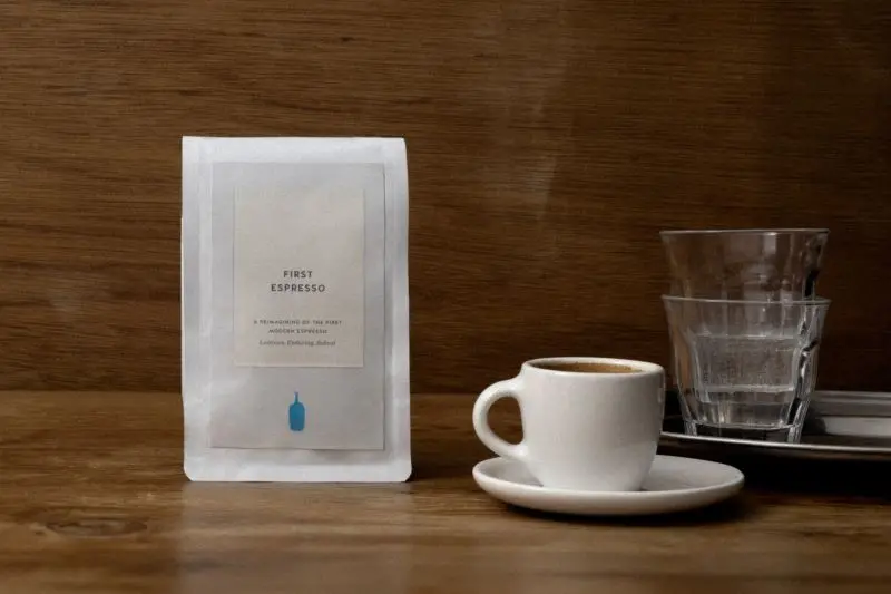 Bag of coffee, espresso cup and water glasses on a table.